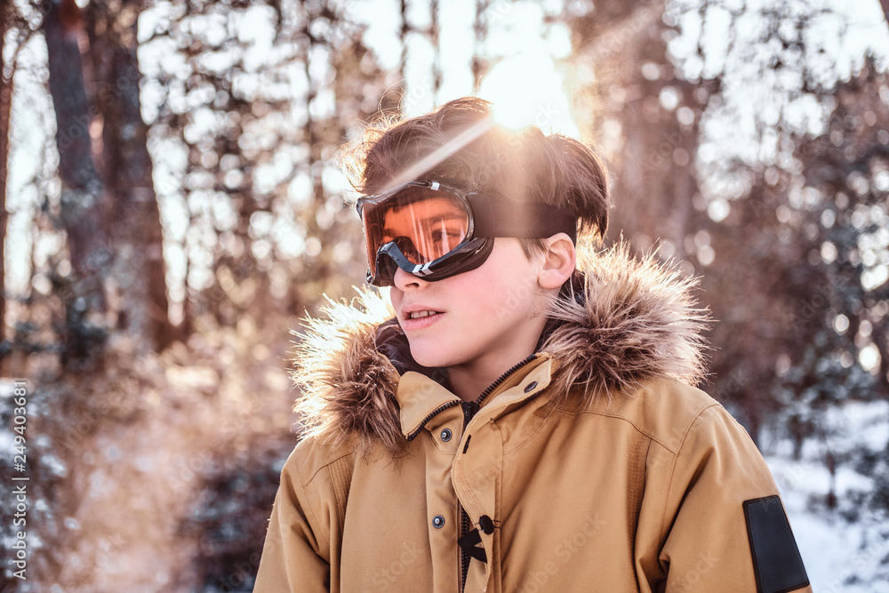 Portrait of a young snowboarder dressed in warm clothes and protective goggles standing in a snowy forest during sunrise Portrait of a young snowboarder dressed in warm clothes and protective goggles standing in a snowy forest during sunrise