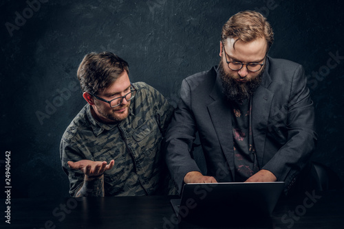 Bearded serious boss checks the presentation of the employee in his laptop on a black background