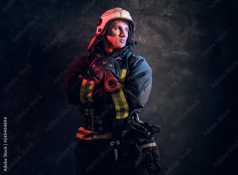 Studio portrait of firefighter in uniform and safety helmet holding an oxygen mask and looking sideways with a confident look. Studio portrait of firefighter in uniform and safety helmet holding an oxygen mask and looking sideways with a confident look.