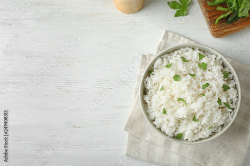Bowl of boiled rice served on wooden table, top view with space for text photo