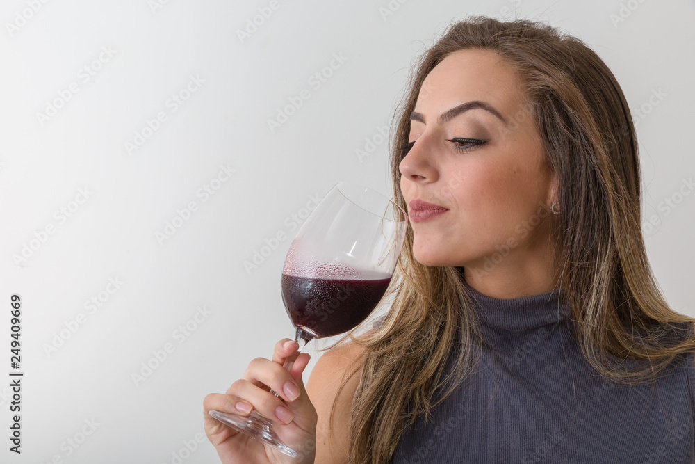 Concentrated young woman sommelier with red wine in glass over white background Concentrated young woman sommelier with red wine in glass over white background