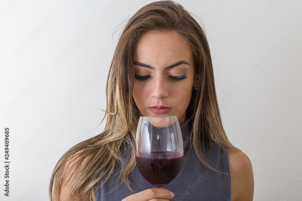Concentrated young woman sommelier with red wine in glass over white background