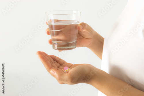 Closeup woman hand with pills medicine tablets and glass of water for headache treatment. Healthcare, medical supplements concept.