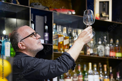 Elderly bartender cleans the glass. A handsome bartender polishes a glass of wine glasses. The concept of service.