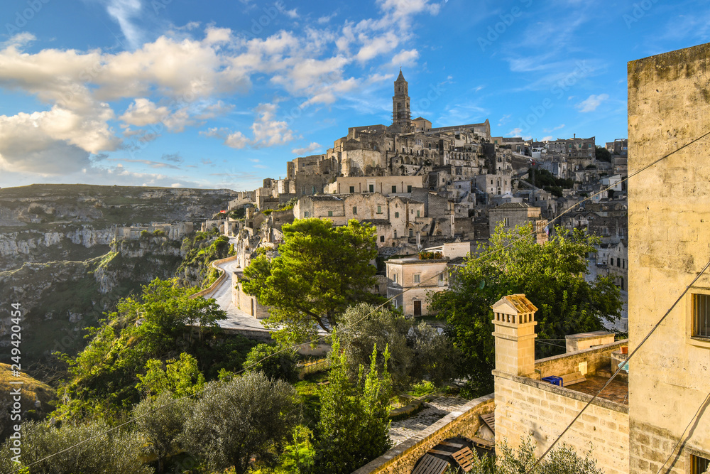 View of the ancient city of Matera, Italy in the Basilicata region, including the old town, tourist street and mountain path, Sasso Barisano tower and the steep ravine canyon below.