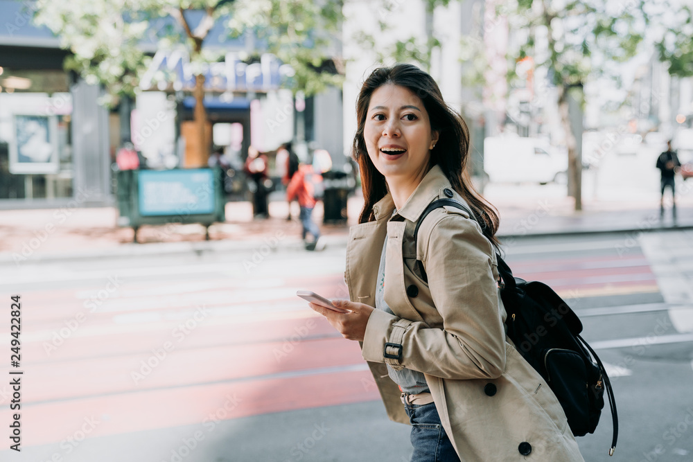 Fototapeta premium travel female backpacker holding cellphone searching route on line map app cheerfully walking on road. beautiful woman tourist using smart phone carrying bag happy sightseeing city san francisco.