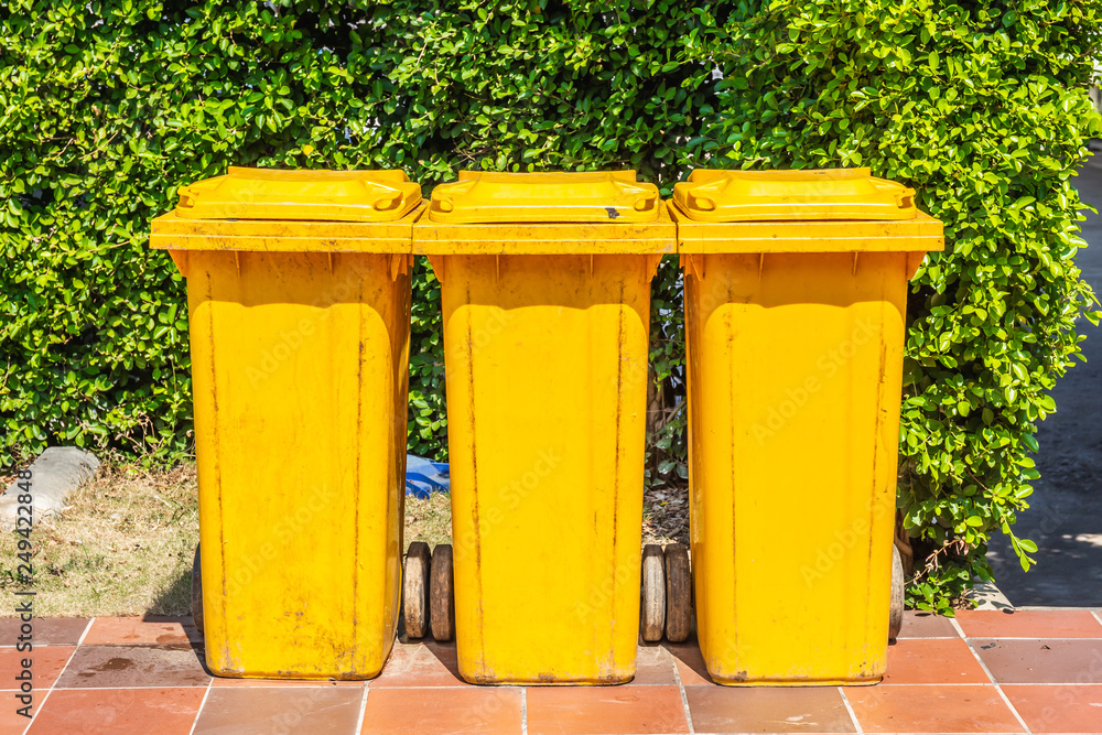 Row of yellow plastic trash bin for wate separation and recycling on green leaf background