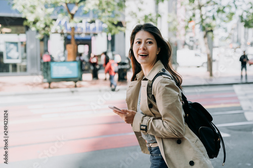 travel female backpacker holding cellphone searching route on line map app cheerfully walking on road. beautiful woman tourist using smart phone carrying bag happy sightseeing city san francisco. © PR Image Factory