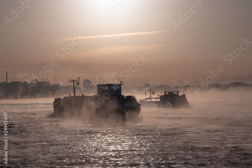 Shipping or cargo river boat on misty water at sunrise.