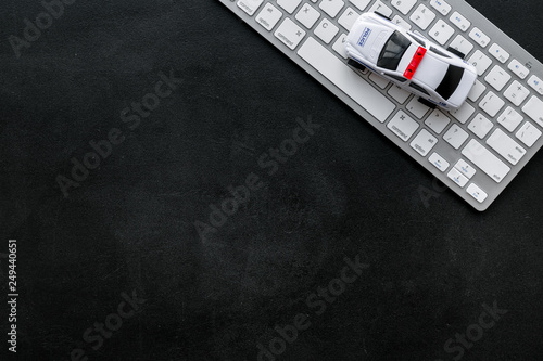 Call police online concept. Police car toy and computer keyboard on black background top view copy space