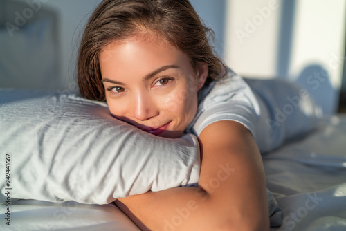 Beautiful Asian woman relaxing at home on pillow bed in bedroom candid smiling portrait. Natural beauty healthy skin model face.