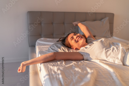 Happy woman lying in comfortable foam latex mattress bed in luxury hotel enjoying relax weekend getaway jumping in bed. Enjoying Asian woman with open arms in freedom.