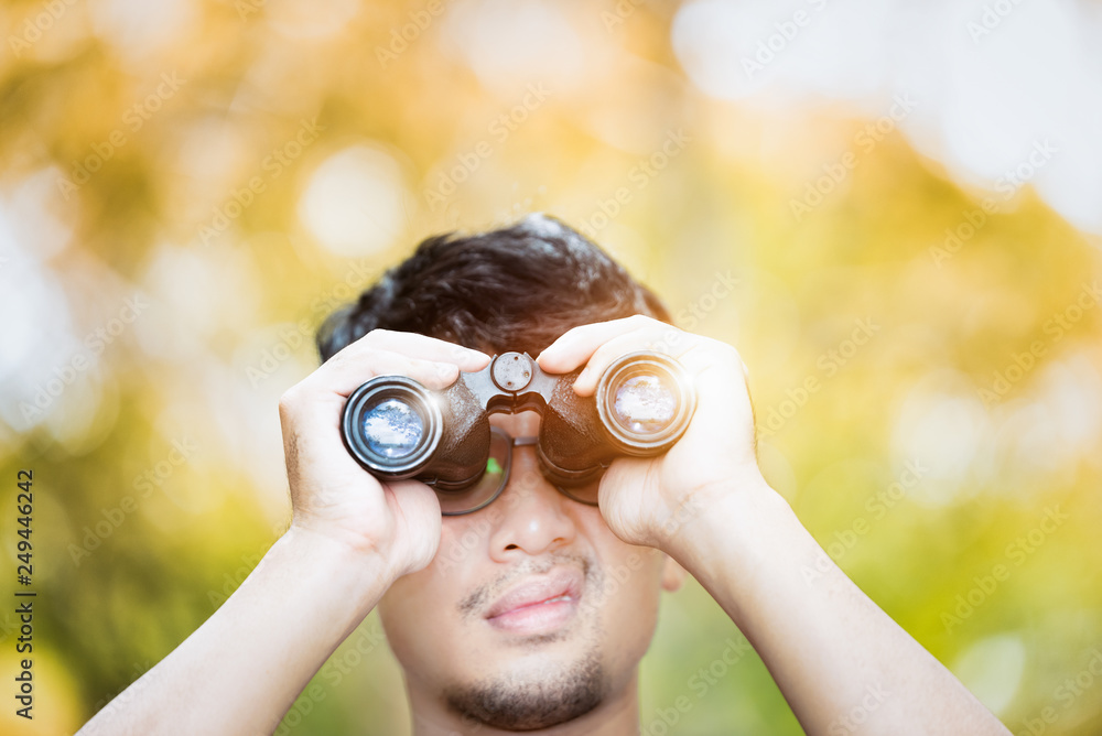 Asian young looking through his binoculars and blinking with sunlight