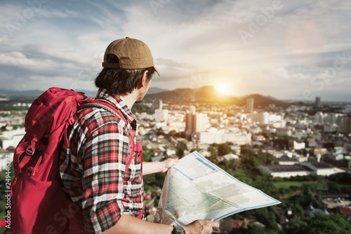 Tourist Traveler Hipster Young Man standing on the peak of natural mountain and rejoices sunset with red backpack and holding map on background valley landscape view.