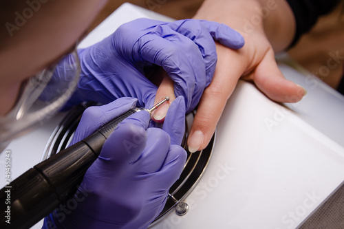 Closeup shot of master in rubber gloves applying an electric nail file drill to trim and remove cuticles in the beauty salon. Perfect nails manicure process. Hardware manicure