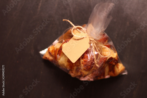 Fresh homemade French croissants with filling in a transparent cellophane bag with a tag on a black table