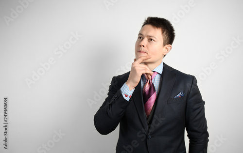 Young businessman in suit on gray background is thinking over question or problem. © Andrii Zastrozhnov