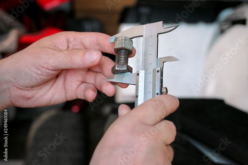 Worker with tools in hands. Mechanic is checking and measuring screw size with stainless steel caliper in automechanics workshop, car garage. Hands of mechanic holding steel screw using steel caliper.