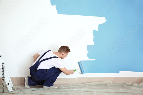 Male painter using roller for refurbishing color of wall indoors