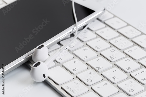 white earphones on white keyboard with phone.