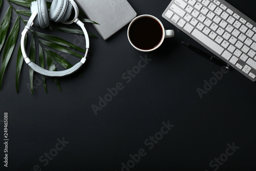Stylish workplace with keyboard, headphones and cup of coffee on dark background photo