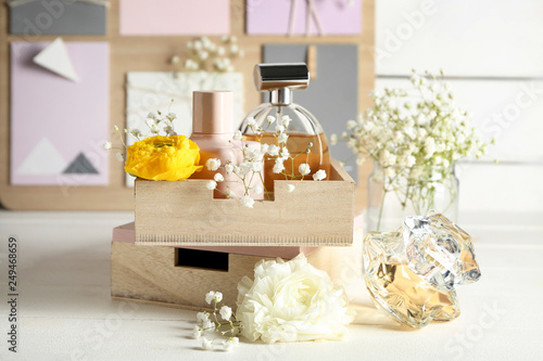 Box with bottles of perfume and flowers on table