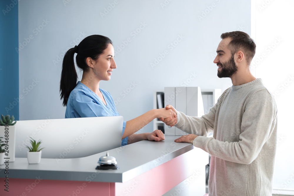Fototapeta premium Young man and female receptionist shaking hands in clinic