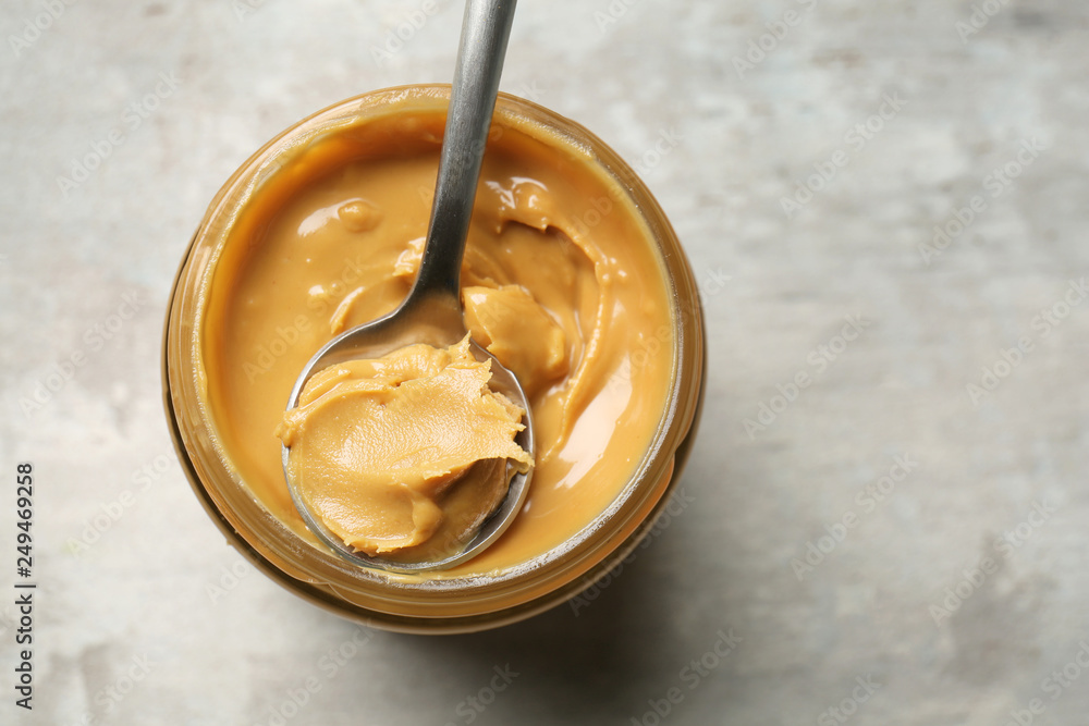 Jar and spoon with tasty peanut butter on grey background Jar and spoon with tasty peanut butter on grey background