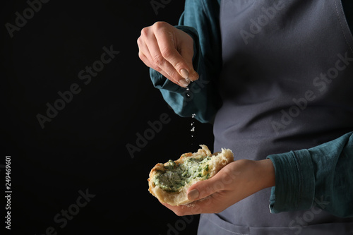 Young woman sprinkling cheese onto piece of fresh bread with green butter against dark background