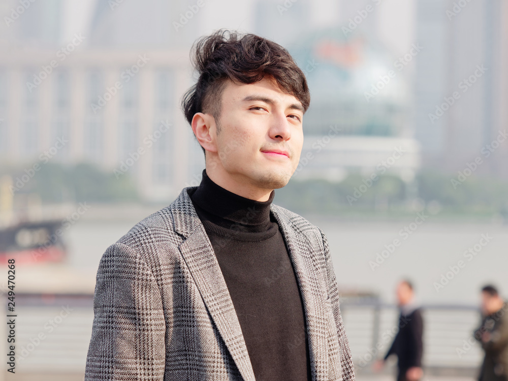 Portrait of a handsome Chinese young man in casual suit smiling and looking at camera confidently with Shanghai bund background, winter fashion, cool young man lifestyle. Portrait of a handsome Chinese young man in casual suit smiling and looking at camera confidently with Shanghai bund background, winter fashion, cool young man lifestyle.