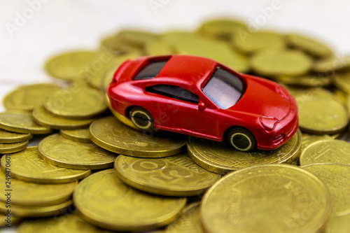 Miniature car model on heap of golden coins on white wooden background