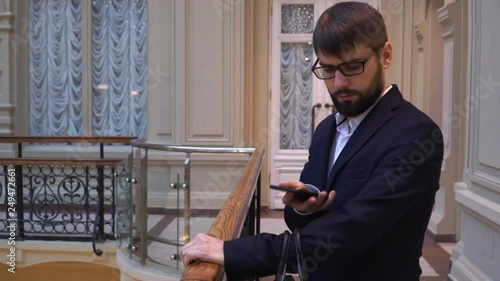 A young attractive businessman with glasses hears a call and answers by mobile phone. Talking on the phone and smiling photo