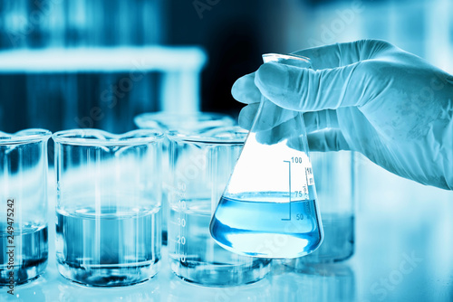 hand of scientist holding flask with lab glassware in chemical laboratory background, science laboratory research and development concept 