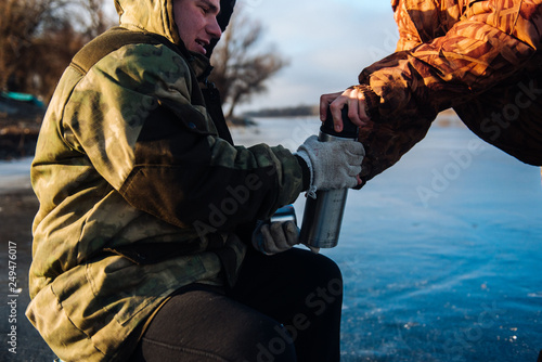 Fisherman pours tea from a thermos in the winter on the ice. Winter fishing