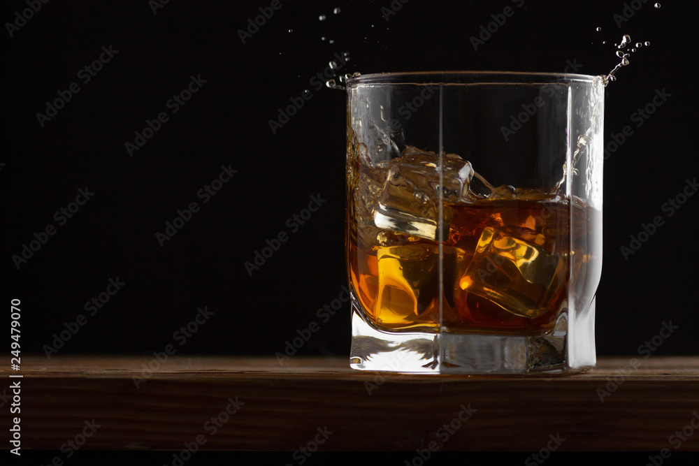 Glass of whiskey with ice cubes on a wooden table and dark background. Glass of whiskey with ice cubes on a wooden table and dark background.