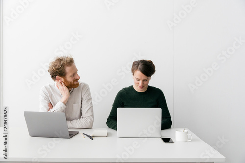 A thirty something couple is working on a laptop in a clean white empty office setting.