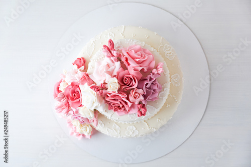 Two-tiered white wedding cake decorated with pink flowers on a white wooden background. Top view.