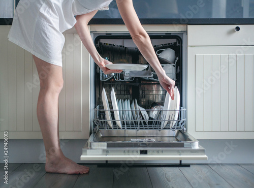 Woman loading dishes into dishwasher, High angle view of utensils in dishwasher at kitchen photo