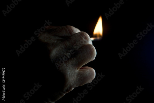 Burning match in old hand on dark background close up