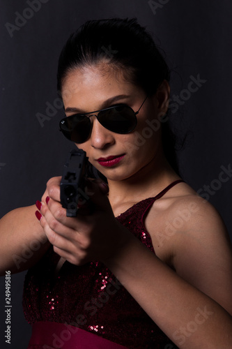 Beautiful Asian caucasian Long straight black hair woman hold gun and point to camera as spy intelligent agency wearing sunglasses, studio lighting dark background shadow