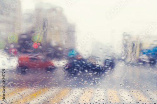 Blurred view through the windshield of a car with raindrops at a crossroad and pedestrian crossing. © flowertiare
