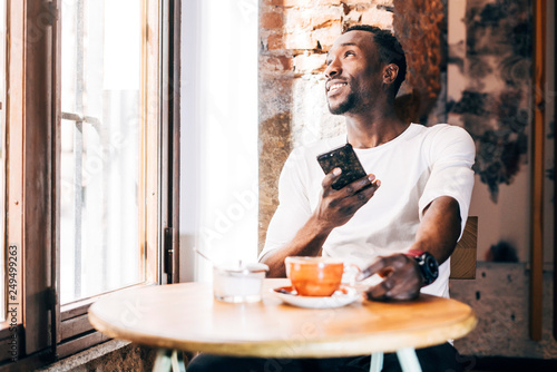 African man consults the cell phone while having a coffee.