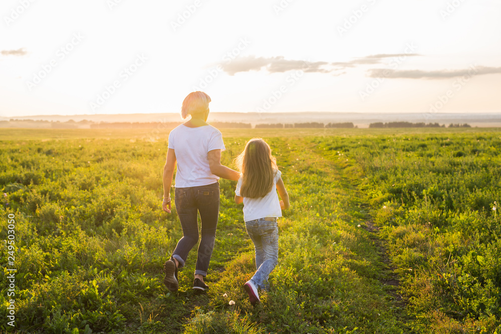 Rear view of mother and daughter running in green field with sunset on background