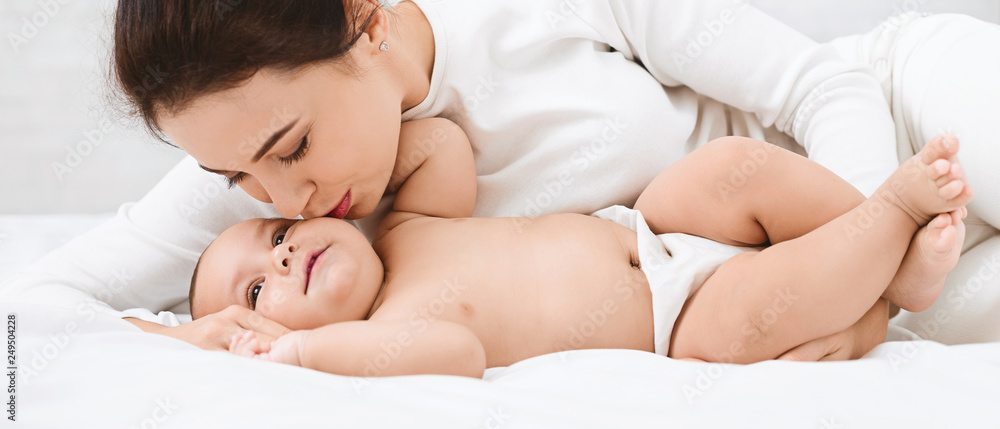 Mother kissing her sweet adorable baby in bed Mother kissing her sweet adorable baby in bed