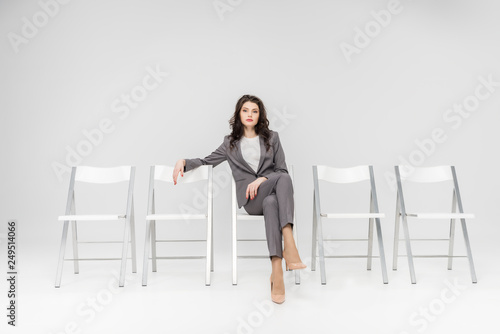 attractive woman sitting with crossed legs on chair isolated on grey