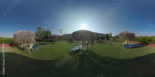 360 VR Video. Green garden and sunbathing area near the hotel. Straw sun umbrellas and empty chaise-longues. Resort in Nea Kallikratia, Greece photo