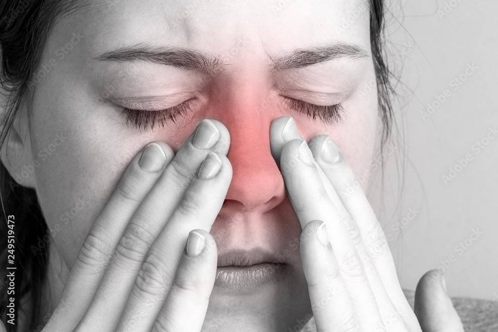 Young woman with sinus pressure pain on gray background. Pain in the nose. Young woman with sinus pressure pain on gray background. Pain in the nose.