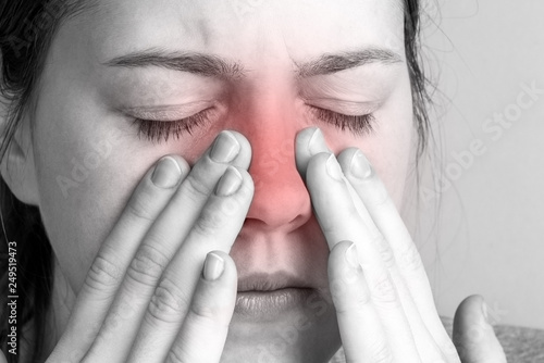 Young woman with sinus pressure pain on gray background. Pain in the nose.  photo