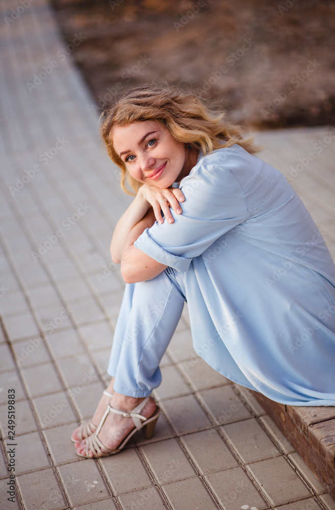 Joyful and cheerful woman in blue wearing and striped t-shirt. Long curly light hair. Wearing stylish blue jacket. Joyful and cheerful woman smiling to camera. Joyful and cheerful woman in blue wearing and striped t-shirt. Long curly light hair. Wearing stylish blue jacket. Joyful and cheerful woman smiling to camera.