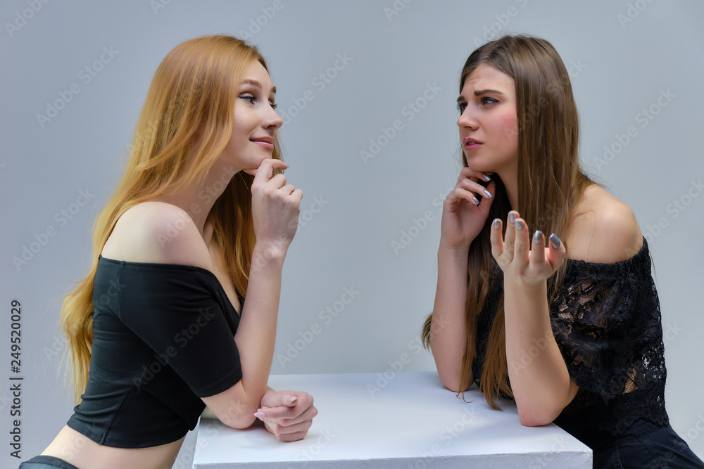 Concept portrait of two cute beautiful girls talking on a gray background in the studio standing at the table Concept portrait of two cute beautiful girls talking on a gray background in the studio standing at the table